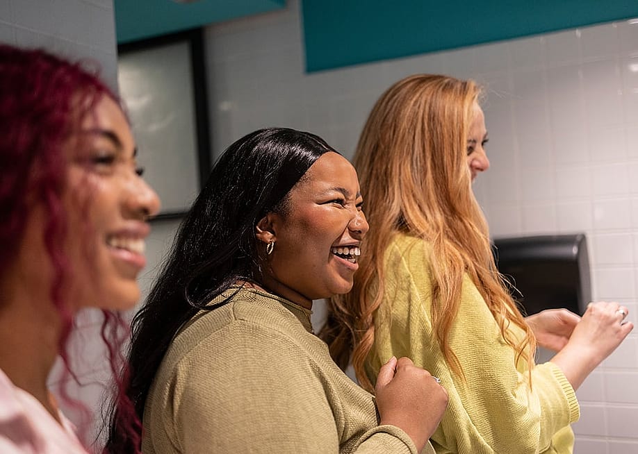 Three young women enjoying a lighthearted moment together in a restroom. — PintoArt // Shutterstock