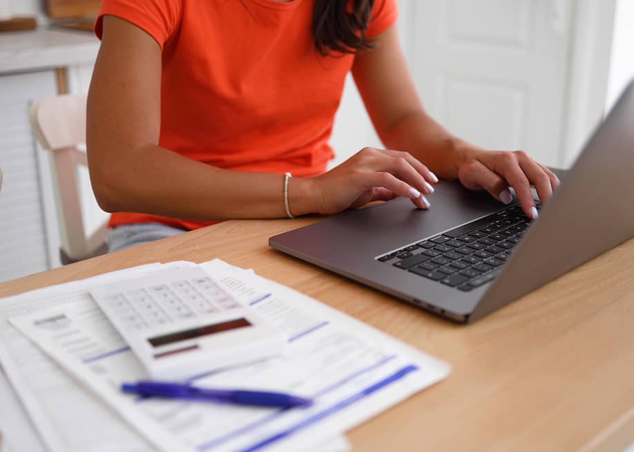 A woman organizing finances at home using a laptop and calculator over documents. — PeopleVideos // Shutterstock