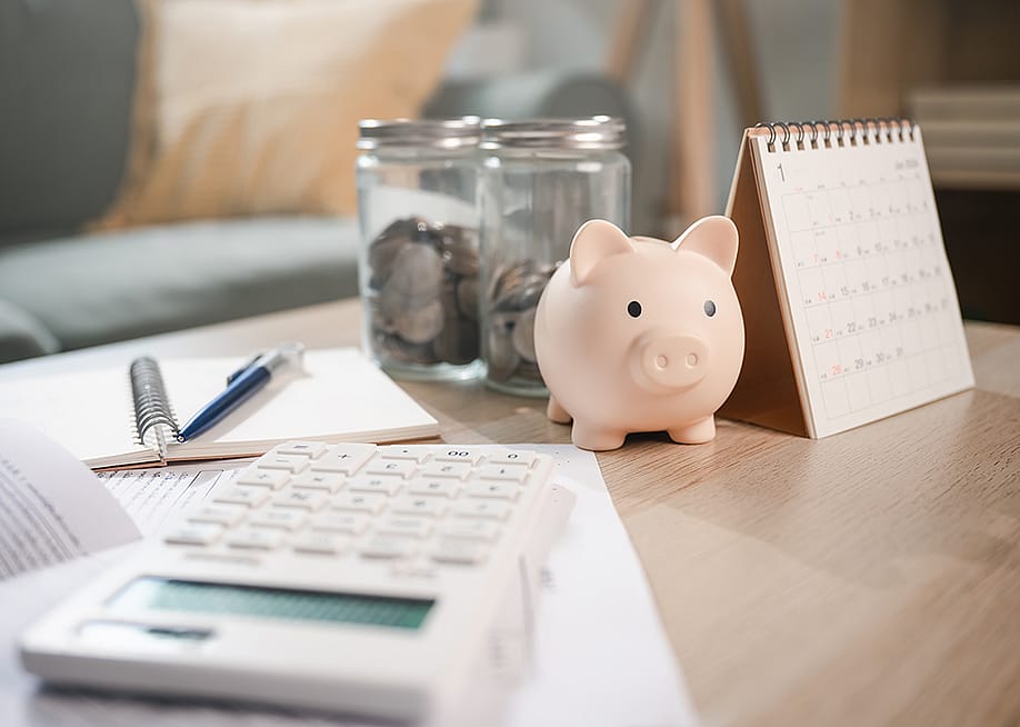 A piggy bank sits on a table with a calculator and a calendar. — Garun .Prdt // Shutterstock