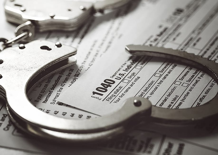 Handcuffs over U.S. tax 1040 forms. — ronstik // Shutterstock