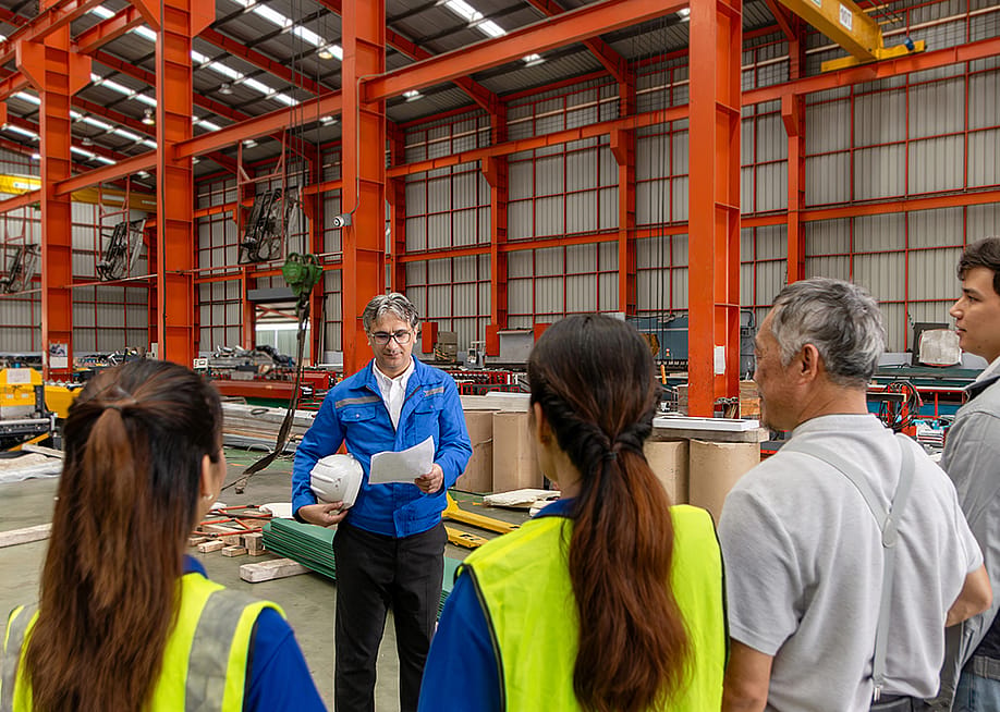A supervisor leads his team for a briefing inside a manufacturing factory. — Stella_E // Shutterstock