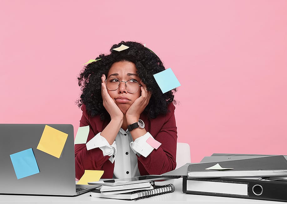 A young woman with sticky notes taped around her looking stressed at work. — New Africa // Shutterstock