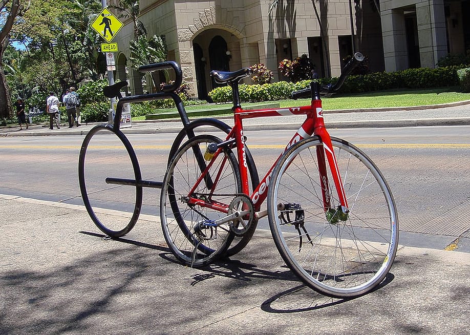 A red racing bicycle locked on a bicycle-shaped parking rack in Honolulu, Hawaii. — Marlon Trottmann // Shutterstock