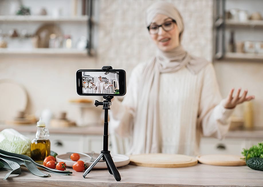 A young woman recording a video for her dieting and food blog using a smartphone on a tripod. — SofikoS // Shutterstock