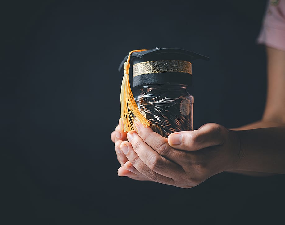 Person holding a jar of coins with a graduation cap as a concept of educational planning. — jd8 // Shutterstock