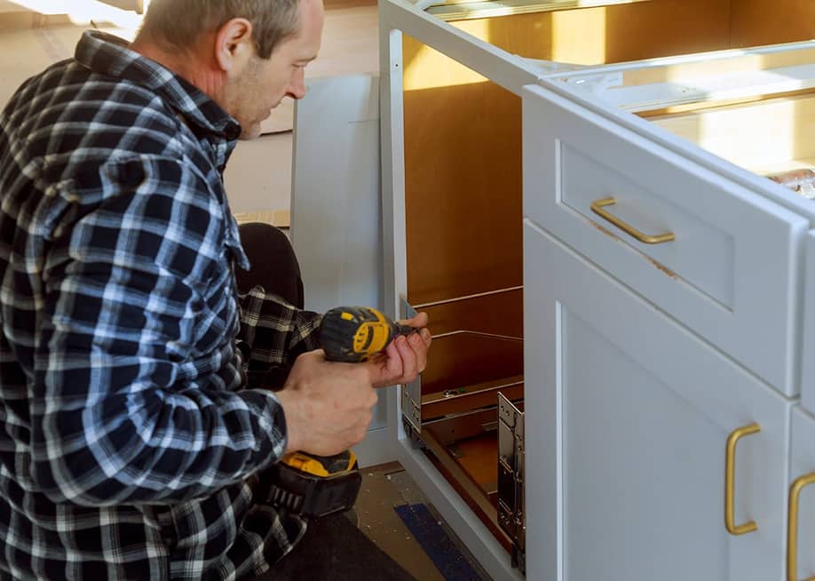 A woodworker installing a drawer for a garbage bin in a kitchen. — ungvar // Shutterstock