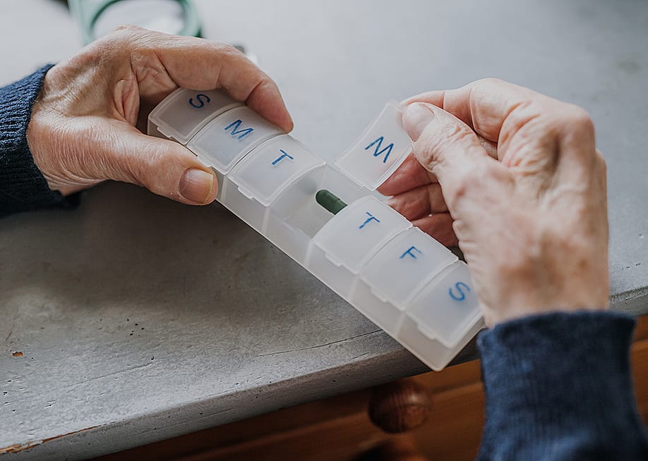 An elderly person arranging medicine in a pill box for the week. — simplystocker // Shutterstock