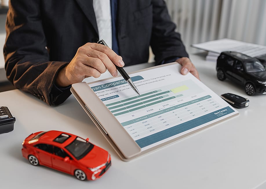 A loan officer showing a car loan comparison document to a client. — ChadaYui // Shutterstock