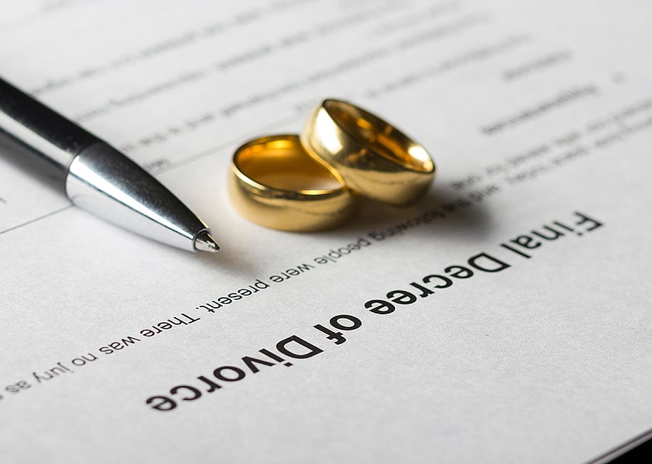 Marriage rings and a pen on top of a divorce decree form. — Roman Motizov // Shutterstock
