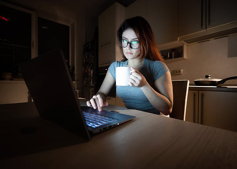 A young female professional working from a home's kitchen at night. — Reshetnikov_art // Shutterstock