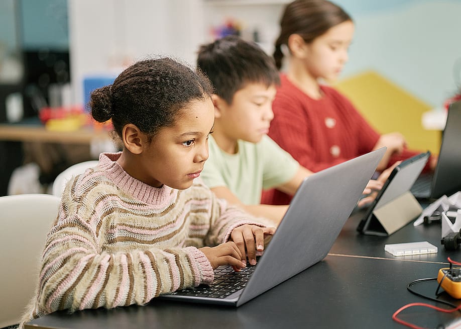 A group of children using laptops in a classroom. — SeventyFour // Shutterstock
