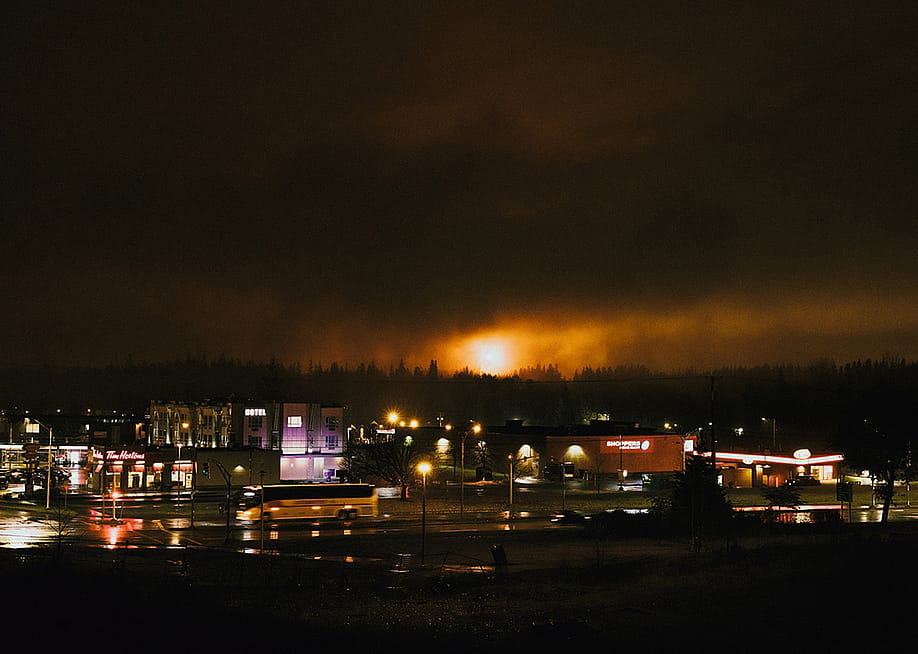 A large flame from a gas flare in Kitimat is visible at night, with the city streets visible in the foreground. — Marty Clemens // The Narwhal