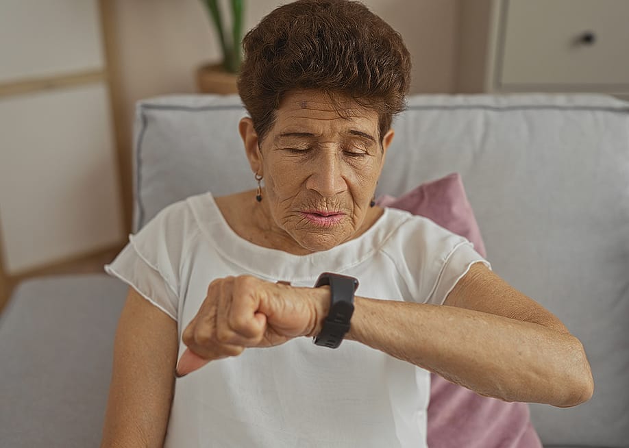 A senior woman observing her smartwatch while sitting on a sofa at home. — Krakenimages.com // Shutterstock
