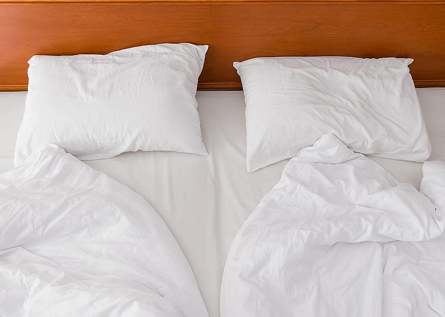 A view from above of an unmade bed with two duvets and white pillows. — Labunskiy Konstantin // Shutterstoc