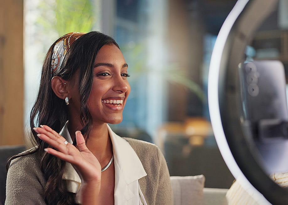 A young female influencer filming a vlog at home using a ring light and smartphone. — PeopleImages // Shutterstock