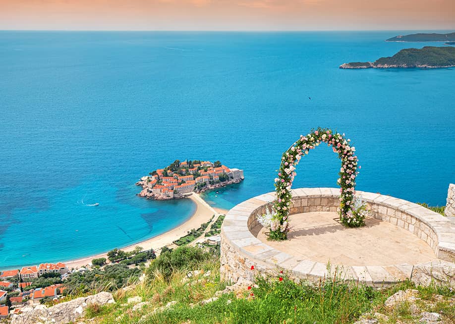 A romantic wedding ceremony at Montenegro Sveti Stefan viewpoint, with an arch adorned in flowers overlooking the Adriatic Sea. — frantic00 // Shutterstock