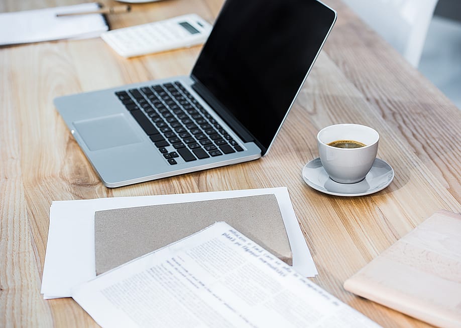 A workplace table with a laptop, coffee, and file documents. — LightField Studios // Shutterstock