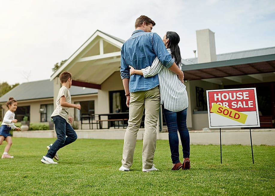 A family of four celebrating on the yard of their new home. — PeopleImages // Shutterstock