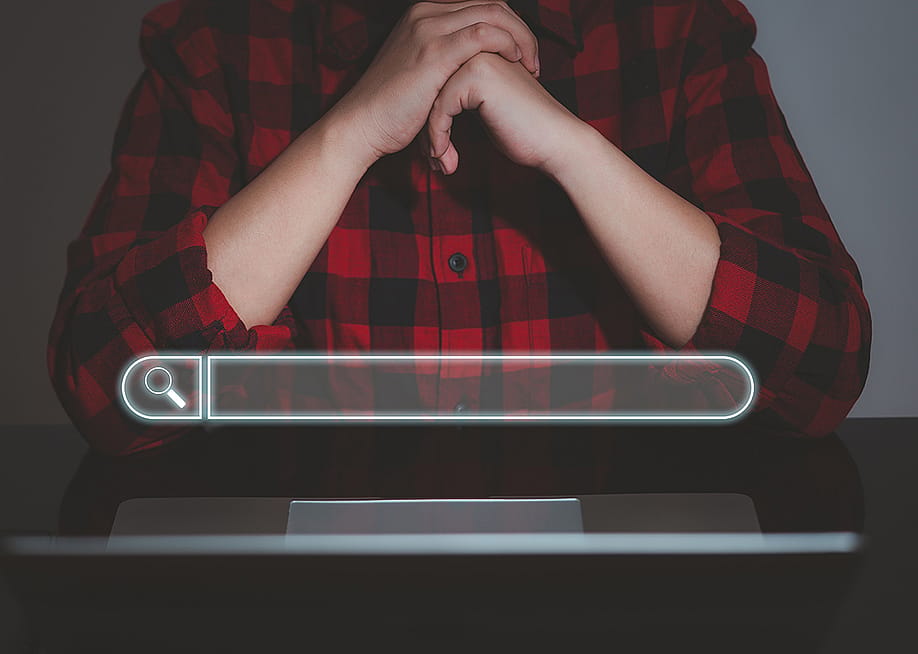 A floating search bar and a data analyst working on search engine concept from a laptop in the background. — bunny pixar // Shutterstock