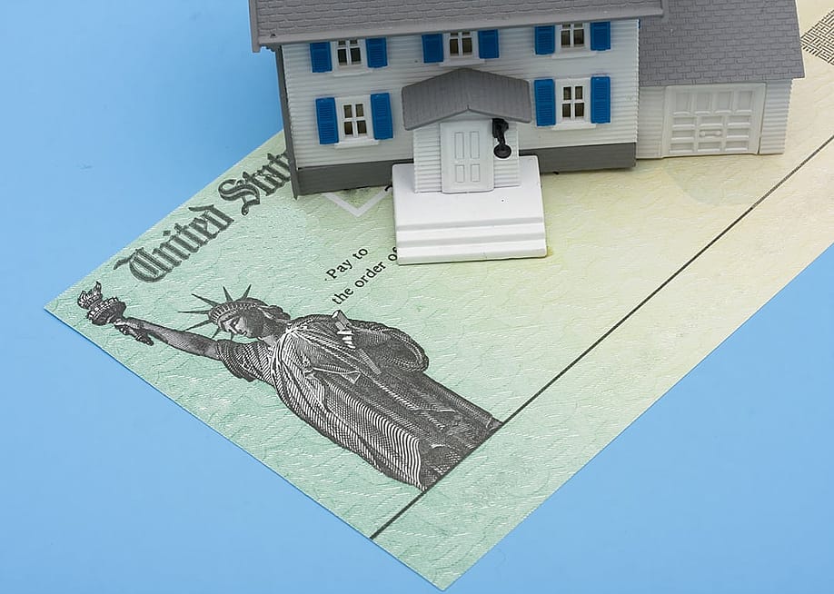 A miniature house placed over a U.S. tax refund check. — karen roach // Shutterstock