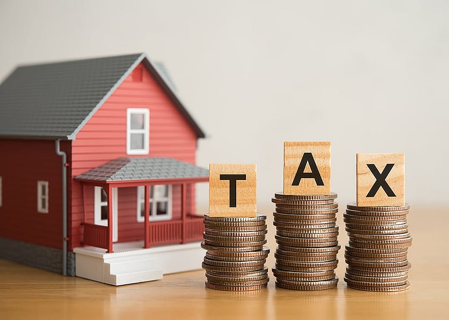 A miniature house and stacks of coins under TAX alphabet blocks. — Pla2na // Shutterstock