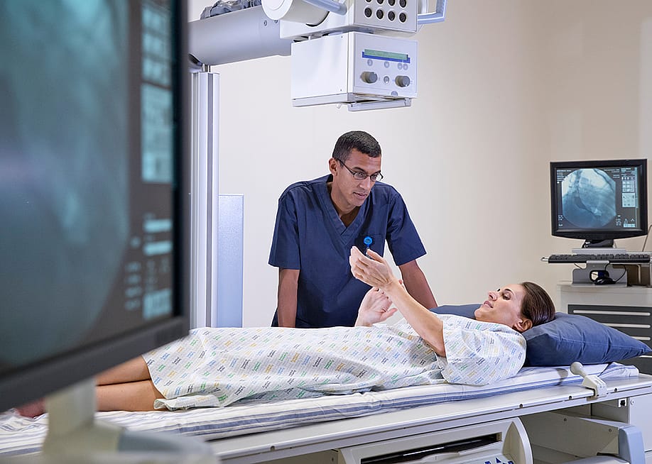A female X-Ray patient consulting with a radiographer during a screening session. — Juice Flair // Shutterstock