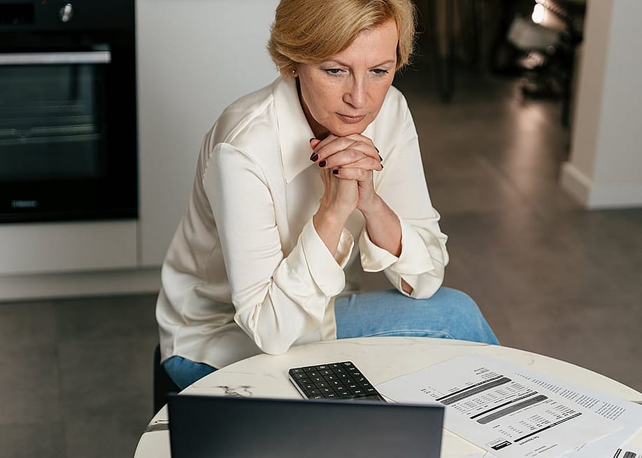 A middle-aged woman carefully looking at financial expenses from a laptop at home. — brizmaker // Shutterstock