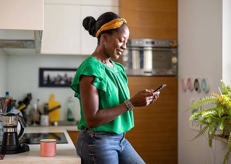 A happy black woman reading messages from smartphone at home. — pikselstock // Shutterstock