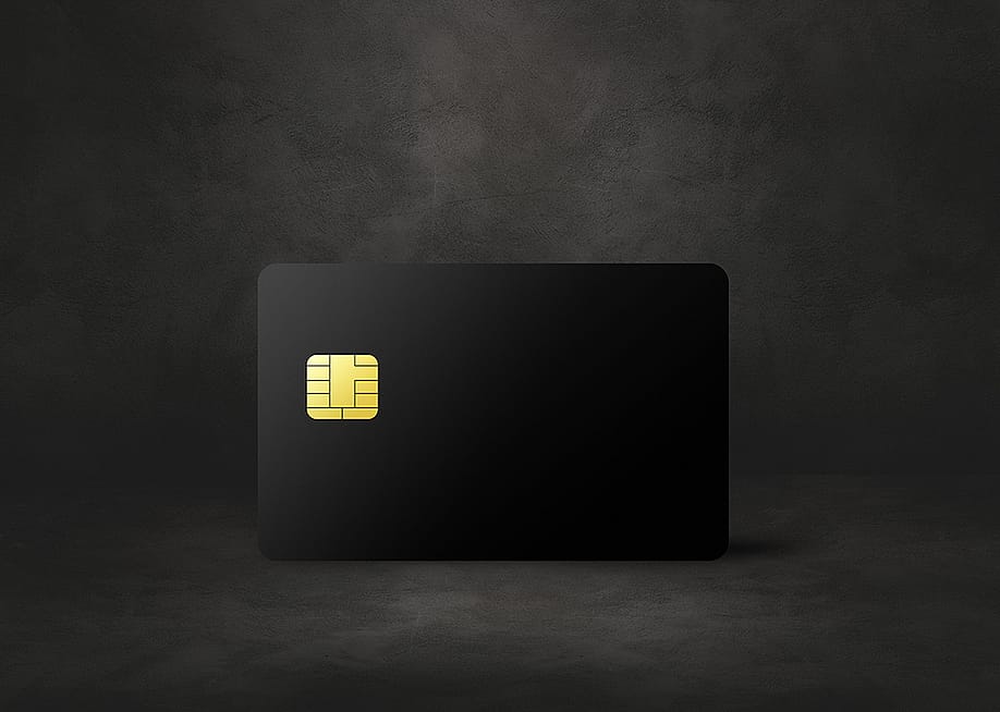 A black credit card in a dark concrete background. — Daboost // Shutterstock