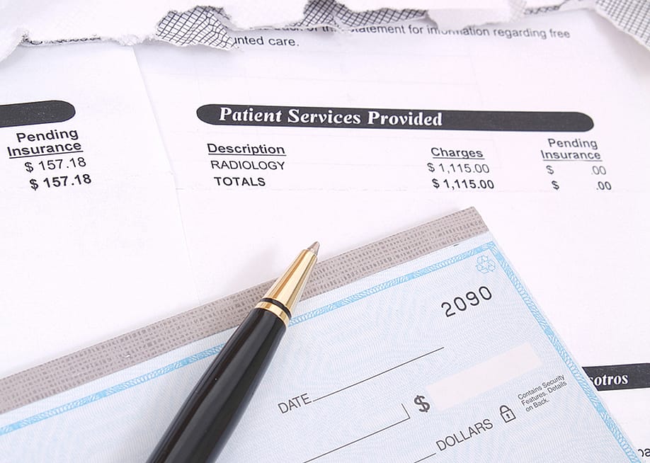 Medical bill statements and a check with a pen. — Jon Schulte // Shutterstock