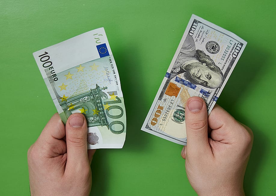 100 Euro and 100 dollar bills held by a person's hands in a green background. — Lanevskyi // Shutterstock