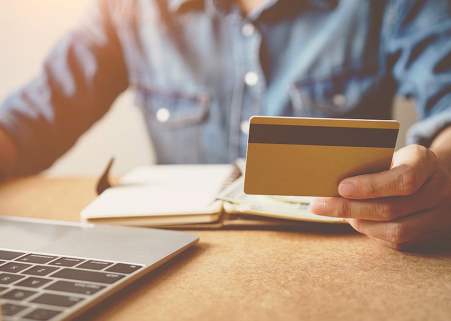A person checking his credit card while reviewing finances from a laptop. — HappyTime19 // Shutterstock