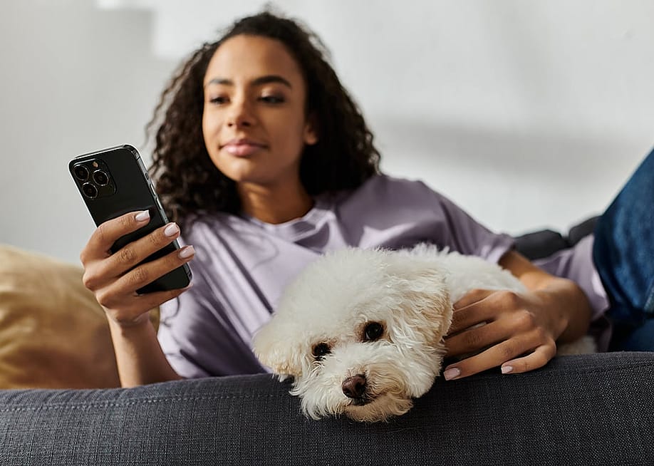 A woman relaxing on the couch while scrolling through her phone and petting her dog. — LightField Studios // Shutterstock