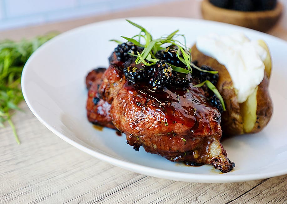 A plate of savory grilled porkchop dish with berry sauce and potatoes. — RPG Brands