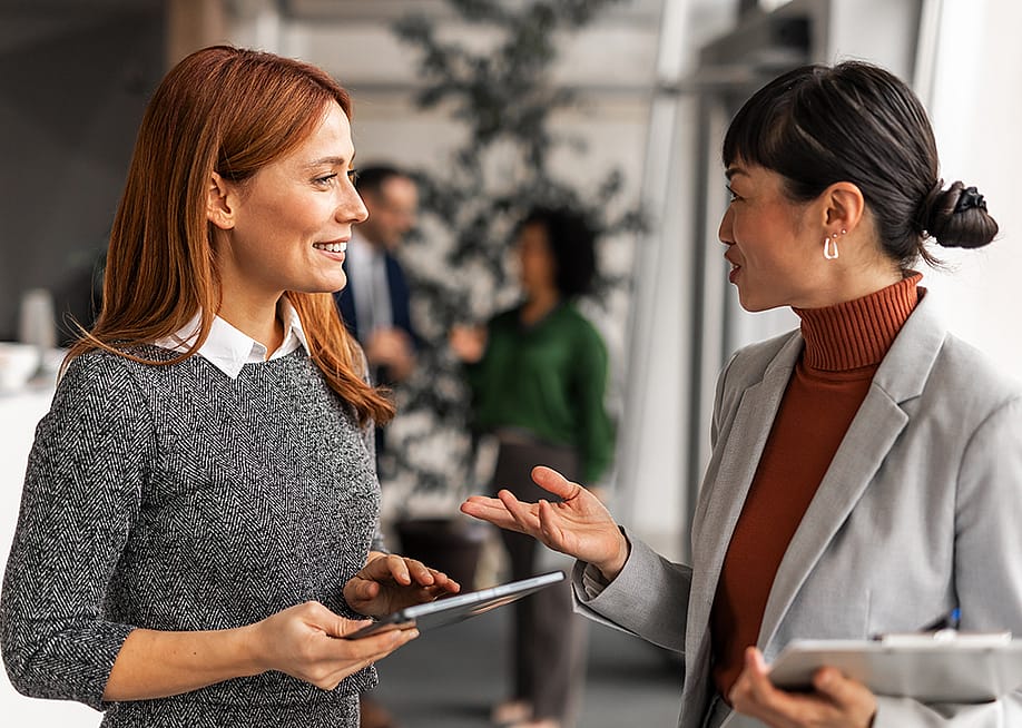 Two female professionals engaged in a positive discussion in an office. — Jelena Zelen // Shutterstock