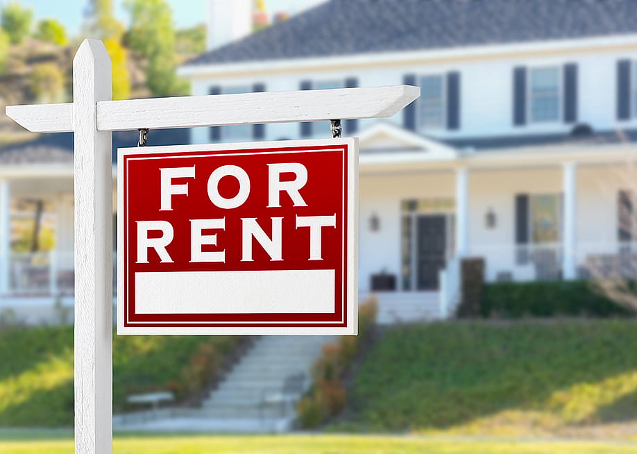 A For Rent sign placed in front of a residential house. — Andy Dean Photography // Shutterstock