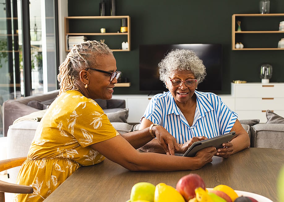 Two senior women sharing to use a tablet in their living room. — wavebreakmedia // Shutterstock