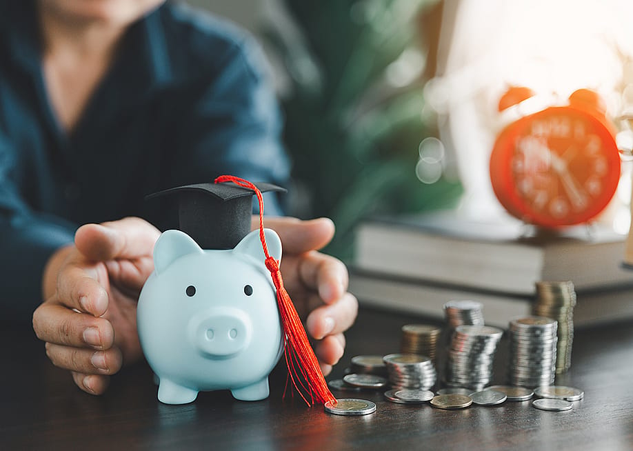 Person protecting a piggy bank with a graduation cap as a concept of saving money for education. — jd8 // Shutterstock