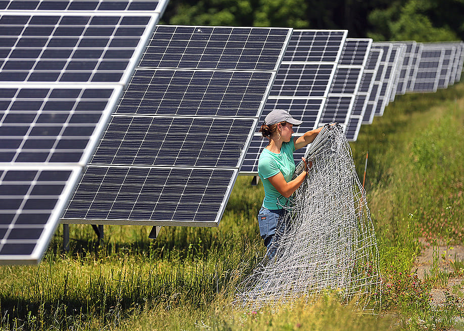 A worker organize fencing materials along solar panels at the Fitchburg Renewables solar farm in Massachusetts. — John Tlumacki // The Boston Globe via Getty Images