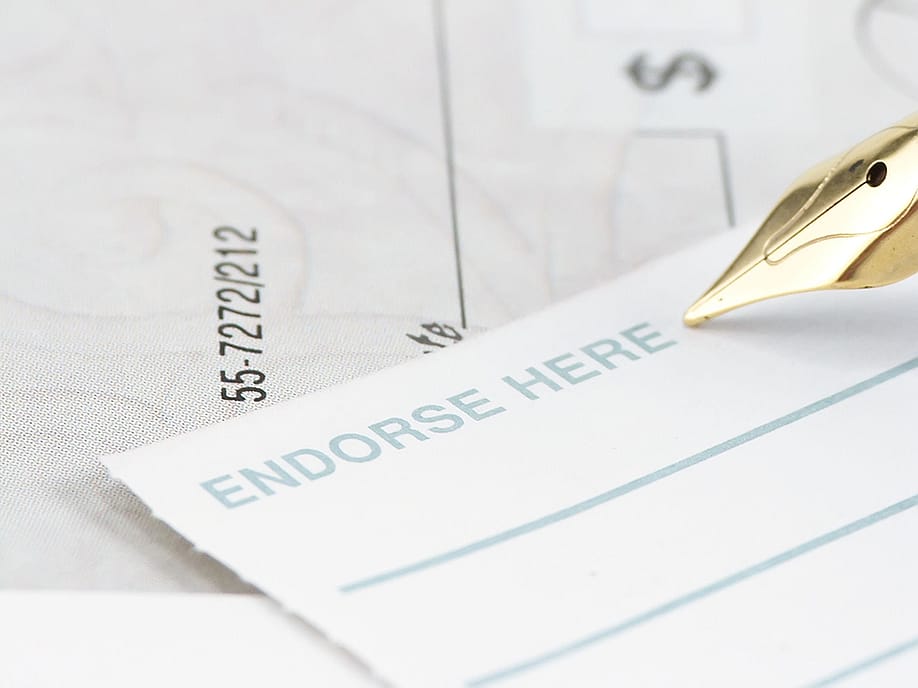 A pen signing an endorsement note to a check. — Margaret M Stewart // Shutterstock