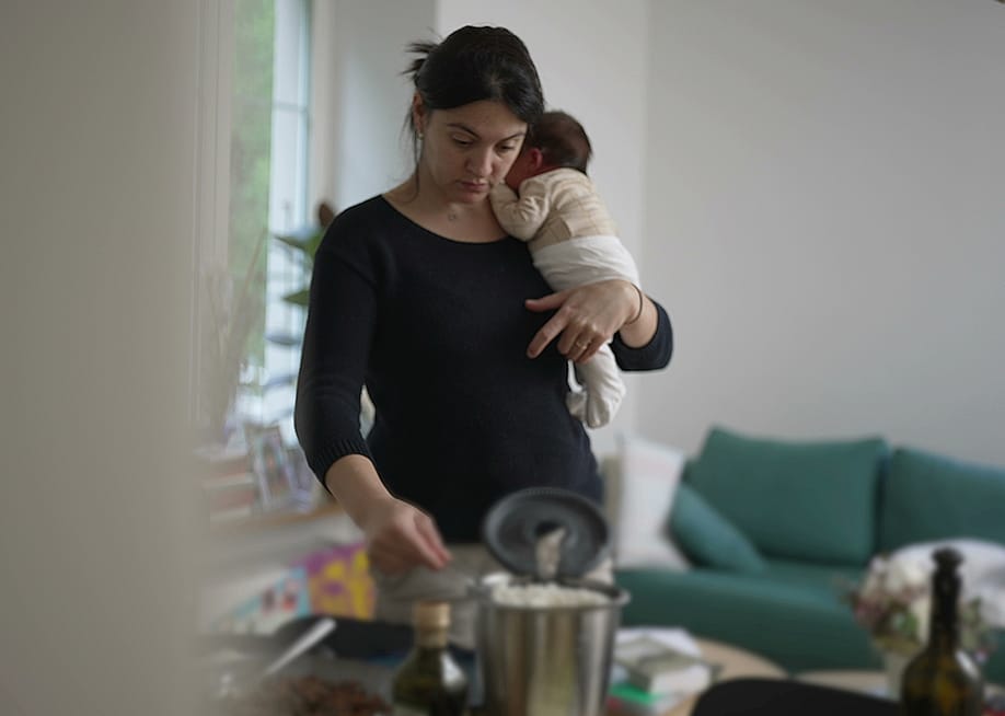 A mother holding her newborn baby multitasking at home. — Bricolage // Shutterstock