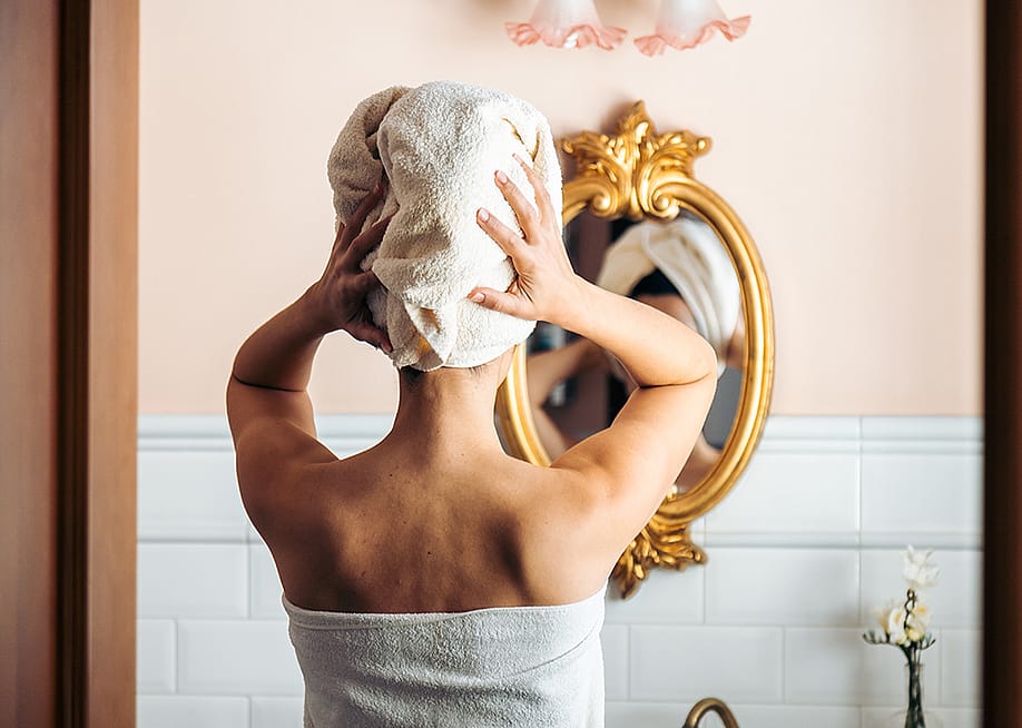 A person drying her hair in front of a mirror from a bathroom. — antoniosantosc // Shutterstock