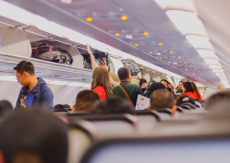 Passengers on a plane storing their carry-on luggage in the overhead compartments. — Asrul_Rowi // Shutterstock