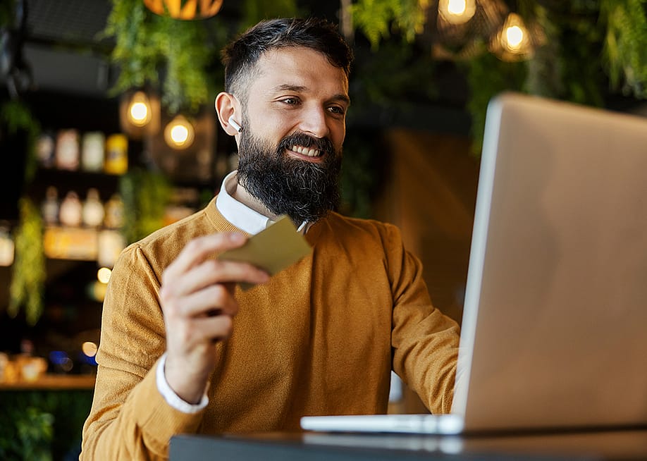 A man in a cafe happily holding a credit card while doing an online transaction. — Dusan Petkovic // Shutterstock