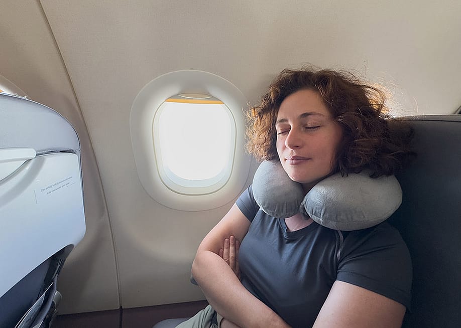 A person sleeping with a neck pillow from her seat in a plane. — Julia Zavalishina // Shutterstock