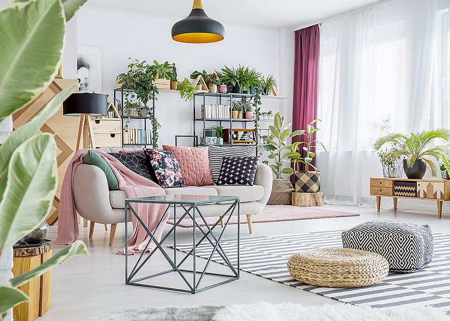 An interior of a spacious living room with plants, poufs, sofas, and cabinets. — Ground Picture // Shutterstock