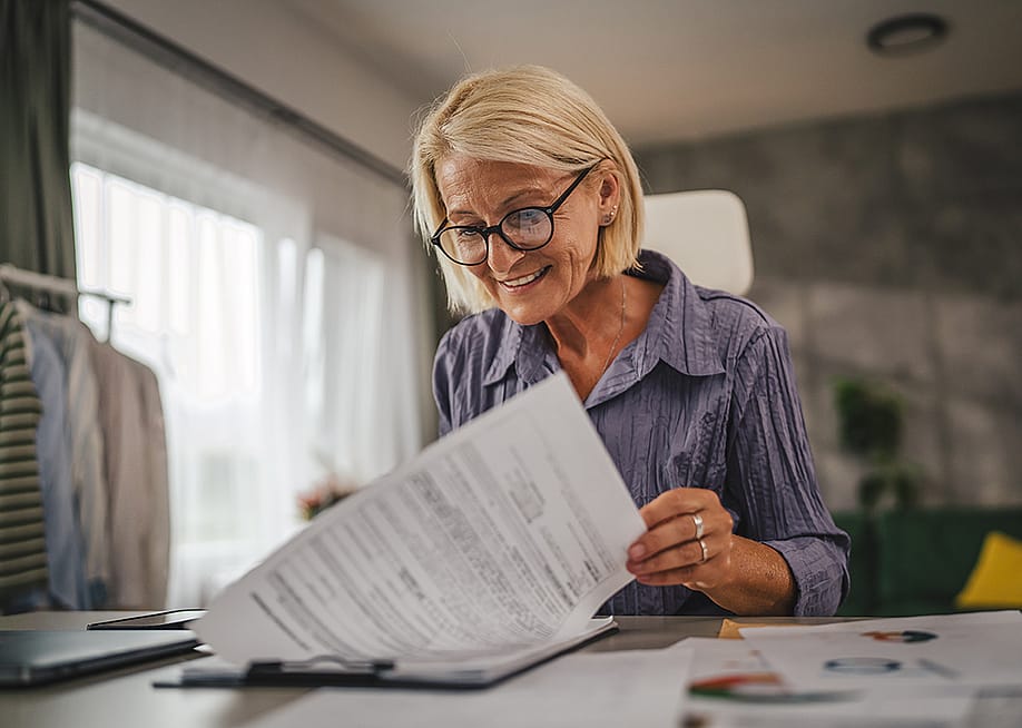 A middle-aged woman reviewing insurance documents at home. — Miljan Zivkovic // Shutterstock