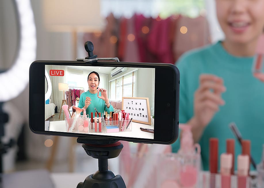An online content creator reviewing cosmetic products live through a social media platform in her home studio. — Chay_Tee // Shutterstock