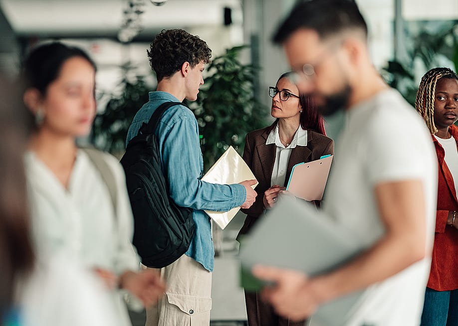 A college student talks to a professor in a campus hallway. — Zamrznuti tonovi // Shutterstock