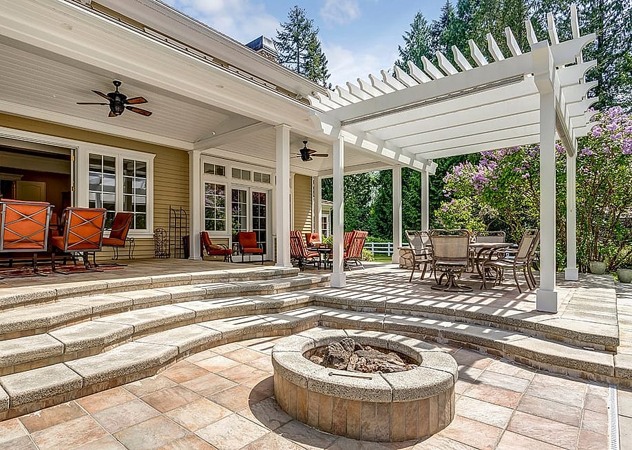 A modern luxury outdoor patio with a white pergola, fire pit, and outdoor sitting area. — Lens Spot // Shutterstock